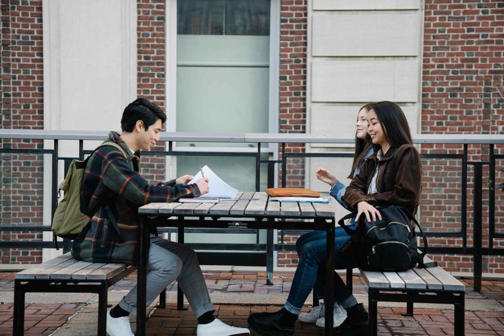 Students sitting outdoors at a table on a school campus.