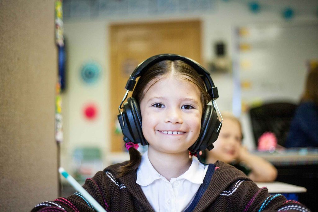 An elementary school aged child wearing headphones smiles 