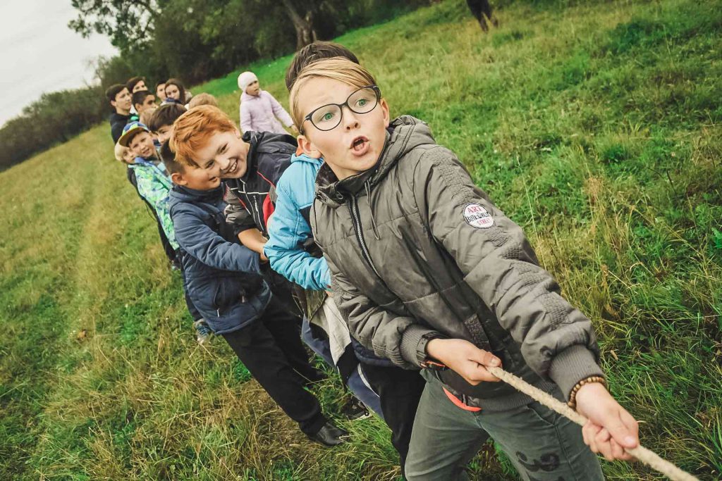 Students engaged in a a tug-of-war activity outside in a grassy field