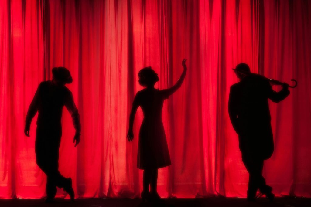 Three silhouettes on a stage behind a red curtain