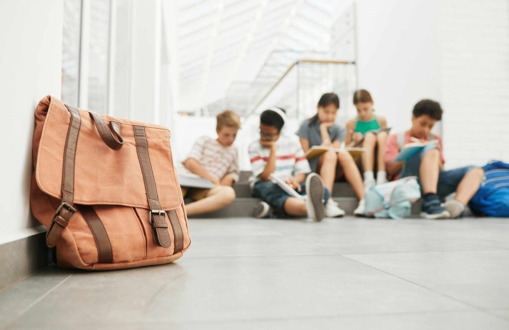 Students gathered around their study materials with a book satchel in the foreground.