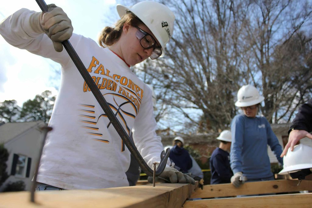 A student volunteering at Habitat for Humanity, or similar organization using building tools.