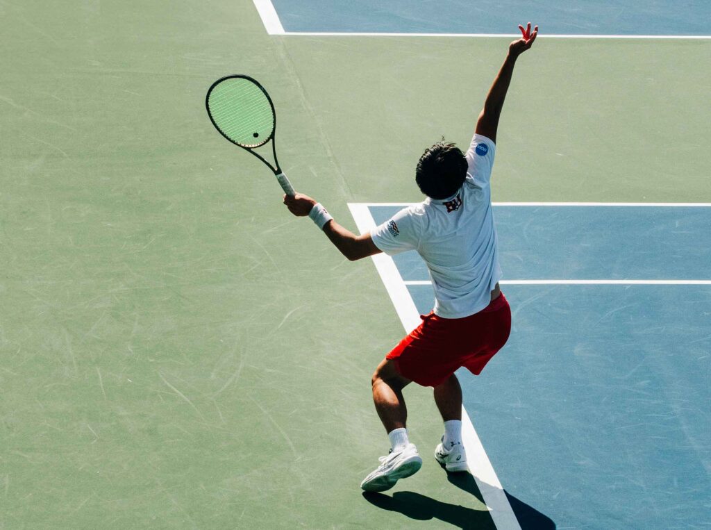 A tennis player throws the ball and readies the racket for a serve.