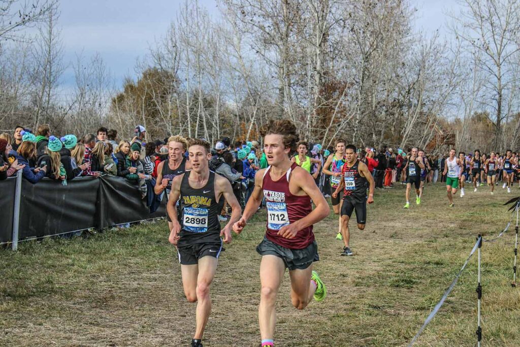A two students compete at a boy's cross country meet while a crowd cheers from the sidelines